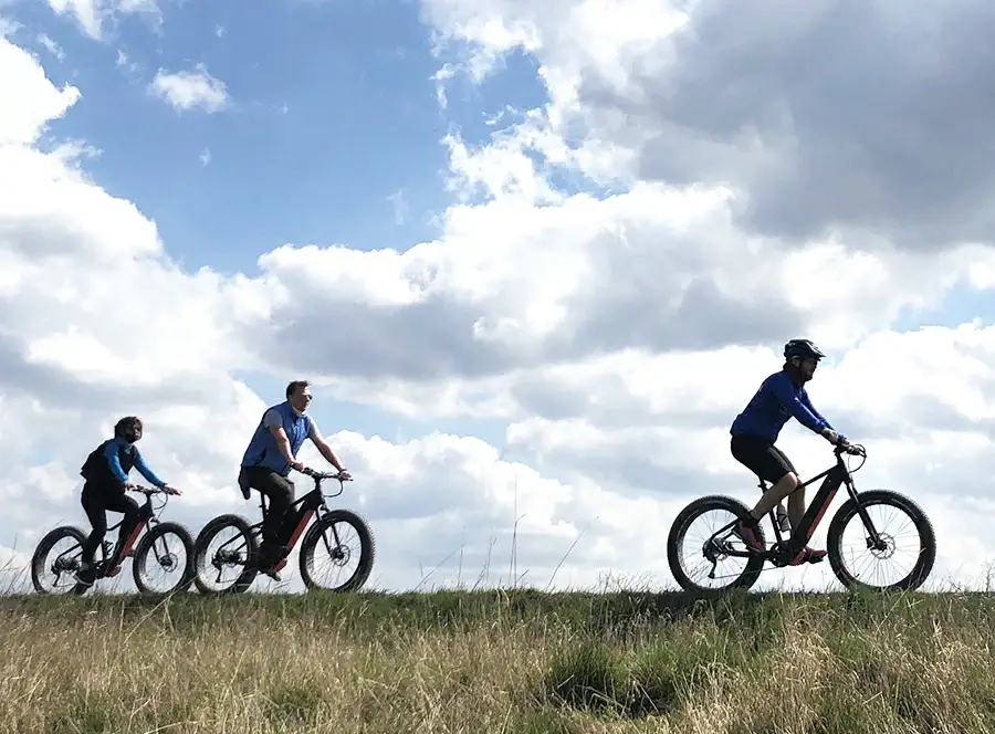 Tři cyklisté na elektrokolech na horizontu